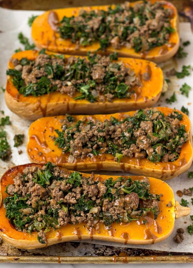 Ground beef stuffed butternut squash with kale and drizzled with tahini sauce on a baking sheet.