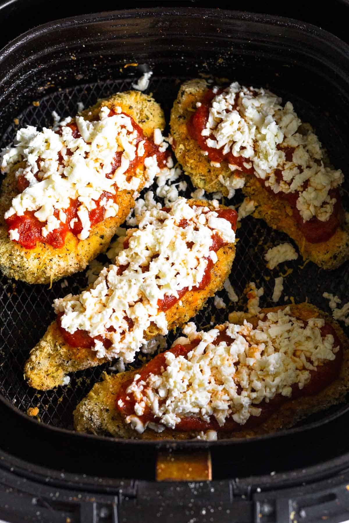 Breaded chicken topped with sauce and cheese in an air fryer basket.