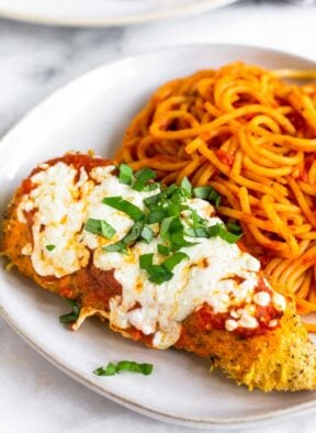A piece of air fryer chicken parmesan on a plate with spaghetti.
