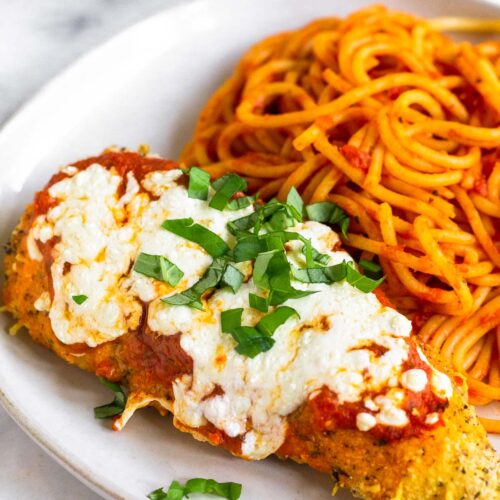 A piece of air fryer chicken parmesan on a plate with spaghetti.