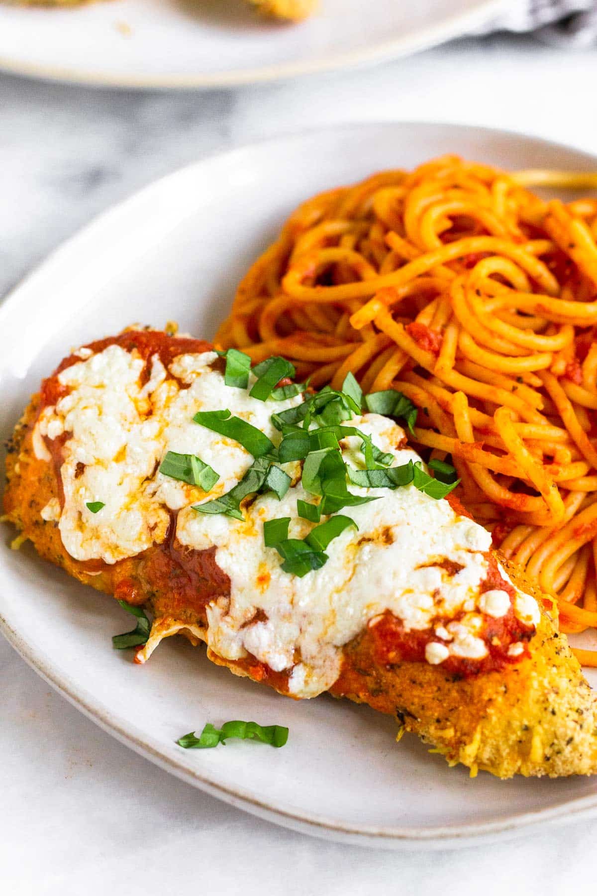 A piece of air fryer chicken parmesan on a plate with spaghetti.