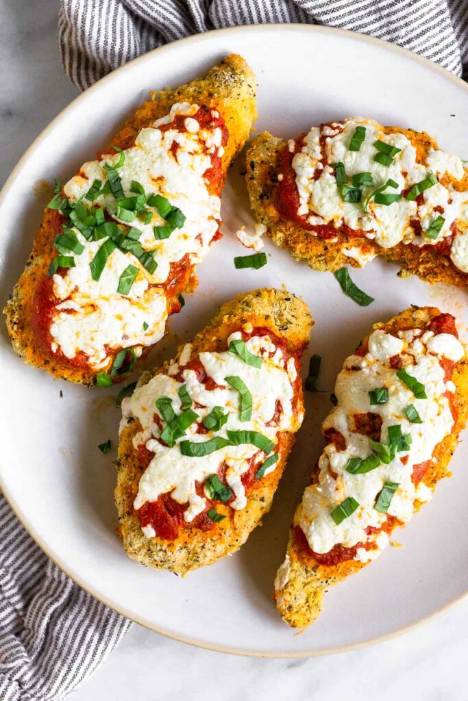 Overhead shot of healthy chicken parmesan on a plate topped with fresh basil.