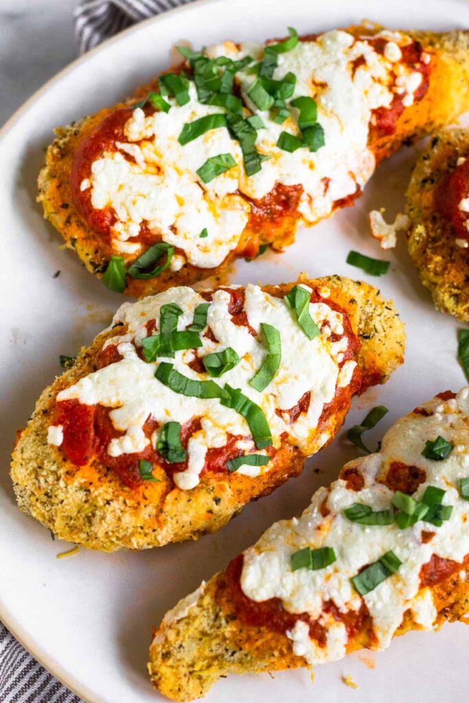 Plate of pieces of chicken parmesan made in the air fryer topped with fresh basil.