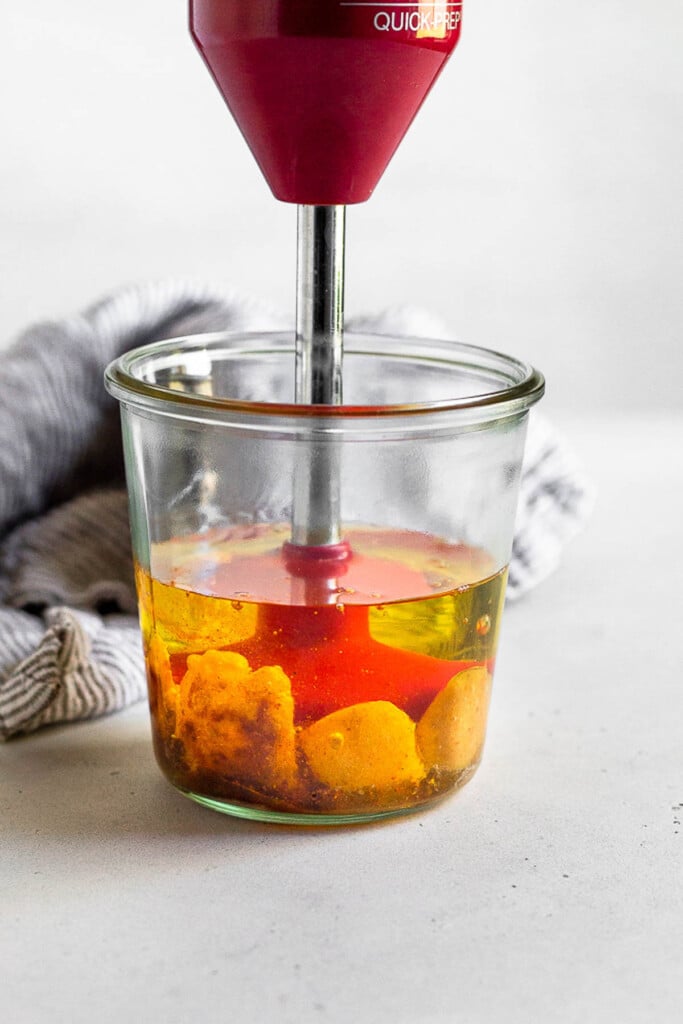 Large jar with an immersion blender in it starting an emulsion for homemade mayonnaise. Behind the jar is a striped kitchen towel.