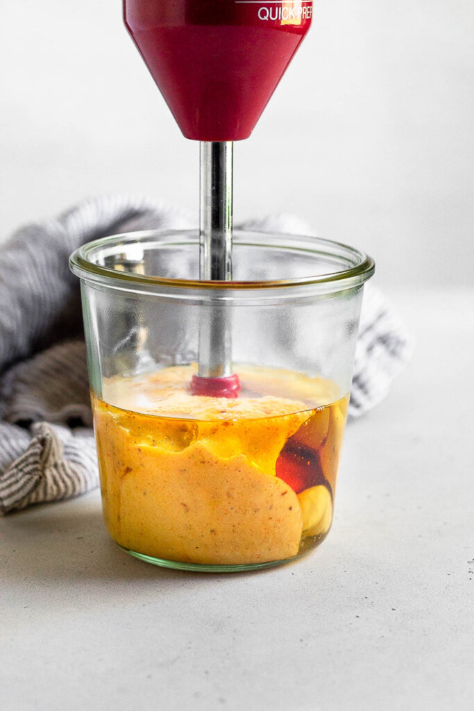 Jar with an immersion blender in it making an emulsion with eggs and oil to make mayo. Behind the jar is a striped kitchen towel.