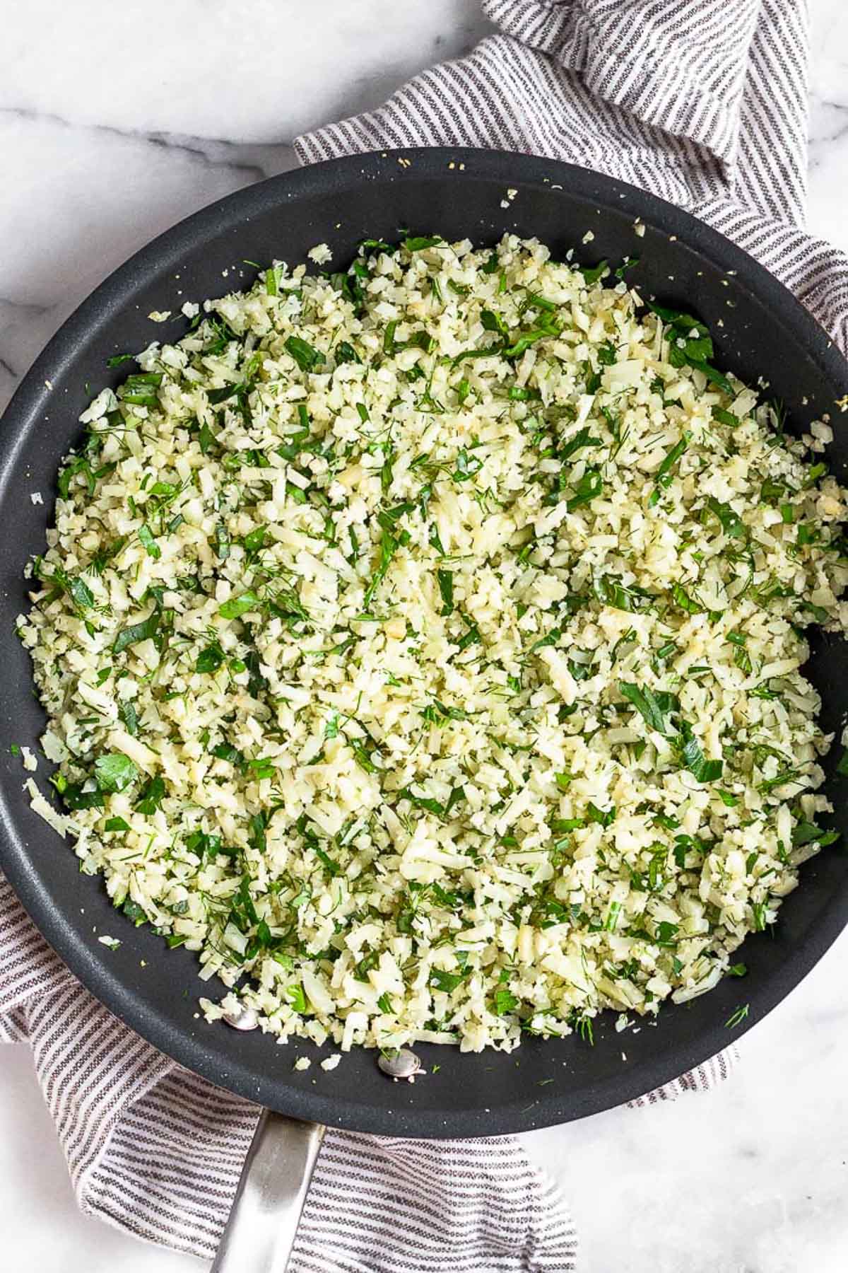 Large saute pan of cooked cauliflower rice with a bunch of herbs mixed in.