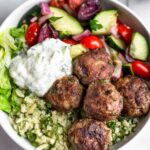Overhead shot of a greek bowl with greek lamb meatballs, herby cauliflower rice, chopped romaine, greek salad, and tzatziki sauce.