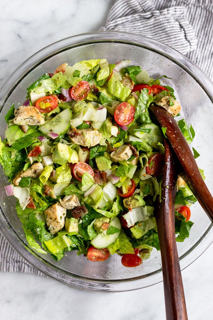Large glass bowl with chopped salad and wooden tongs in it.