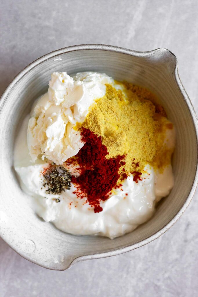 Bowl filled with greek yogurt, cream cheese, nutritional yeast, paprika, and salt and pepper.