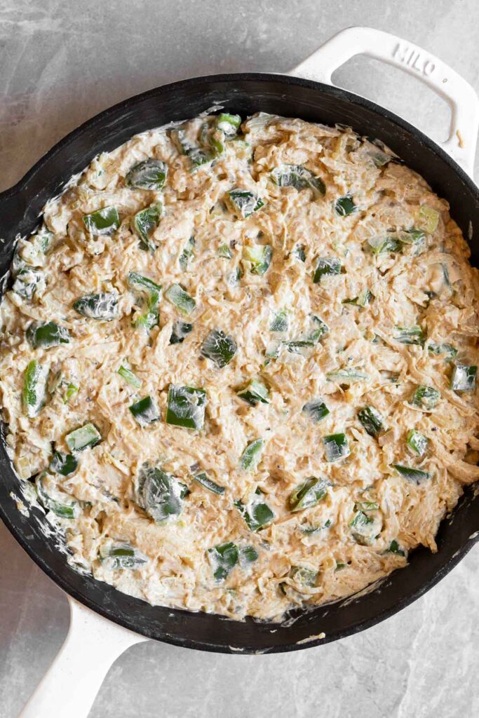 Cast iron skillet filled with a mixture of cream cheese, veggies, and shredded chicken before it is baked.