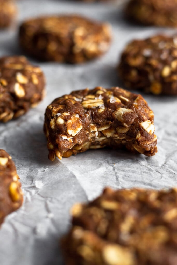 No bake protein cookies on a piece of parchment paper. The cookie in the middle has a bite taken out of it.