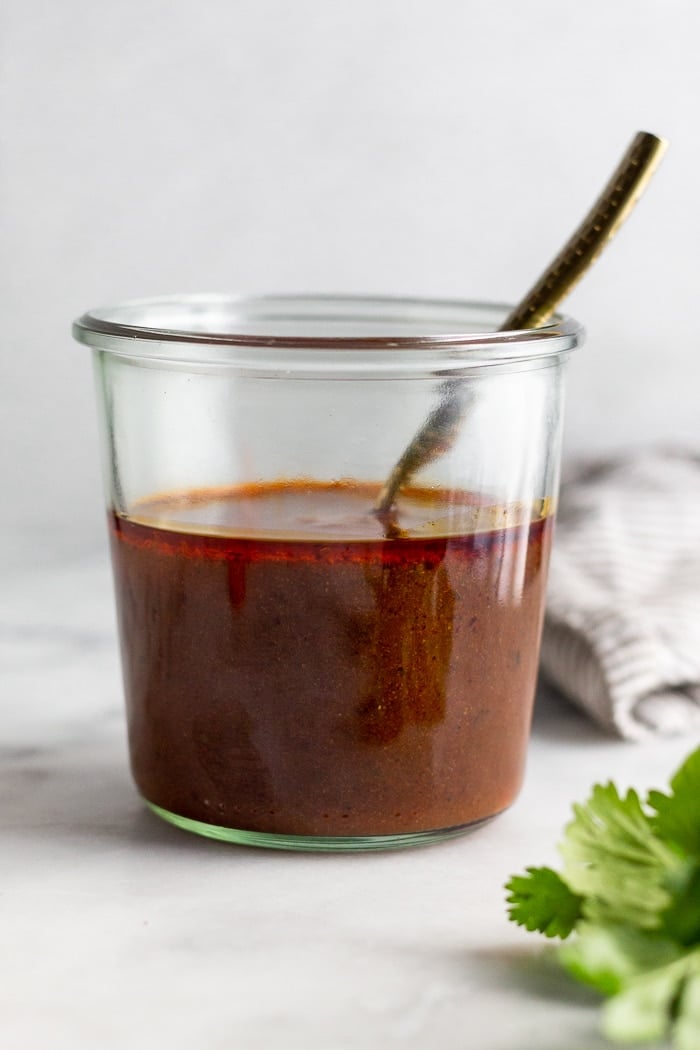 Jar filled with easy enchilada sauce with a spoon coming out of it.