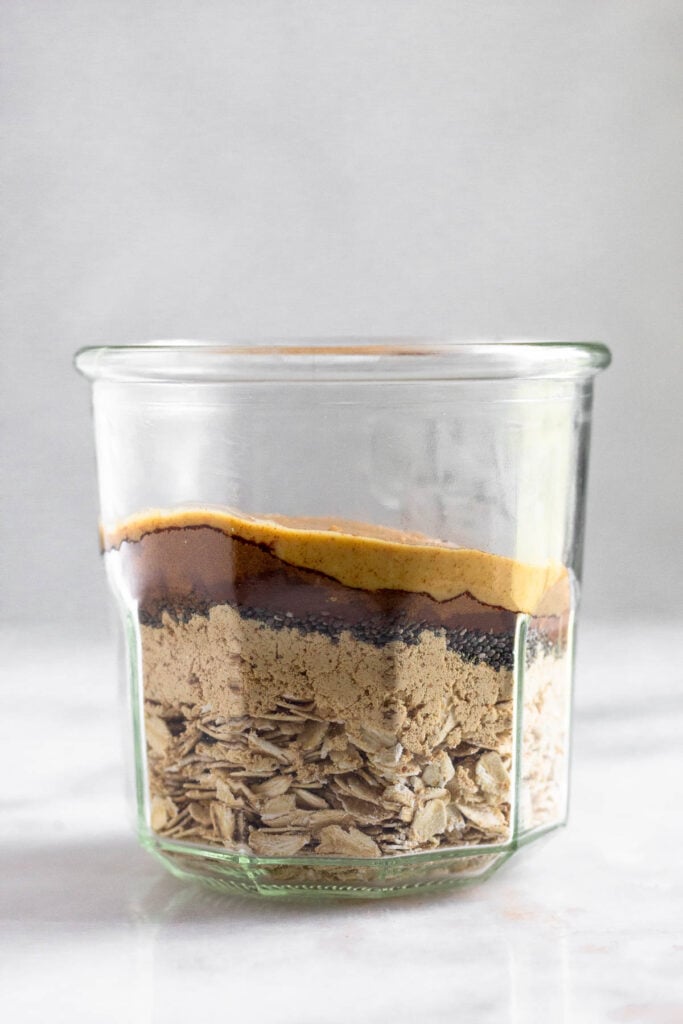 Jar filled with rolled oats, protein powder, chia seeds, cocoa powder, and peanut butter.