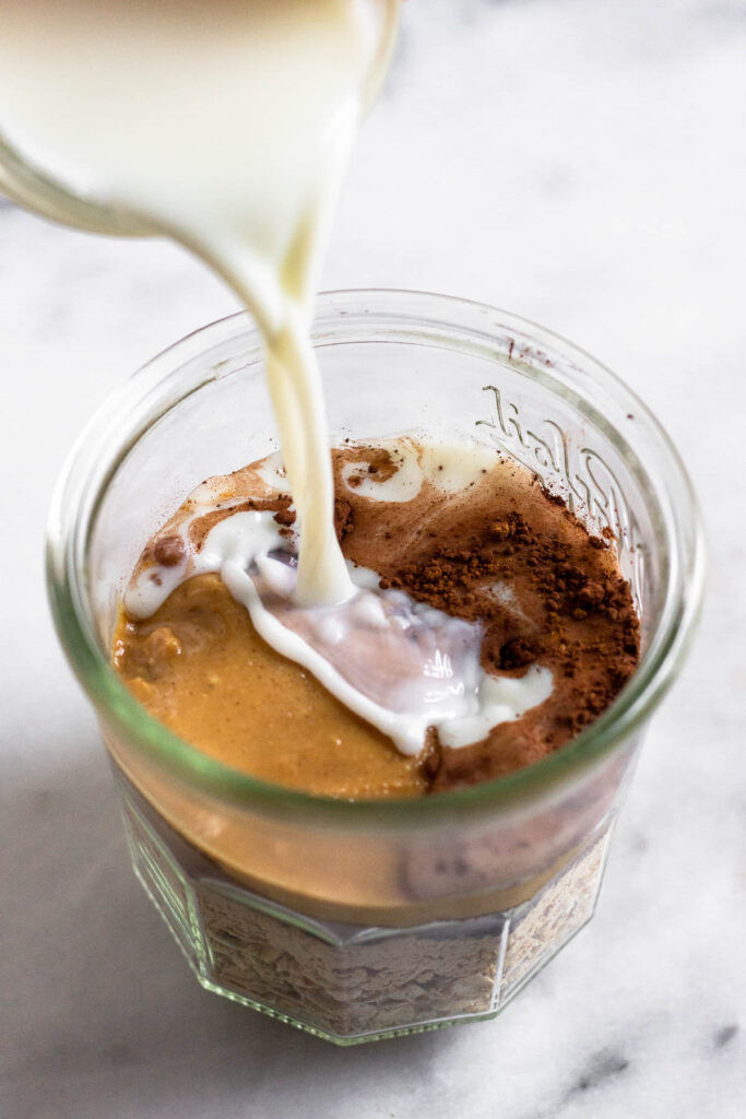 Milk being poured into a jar with oats, peanut butter, and cocoa powder in it.