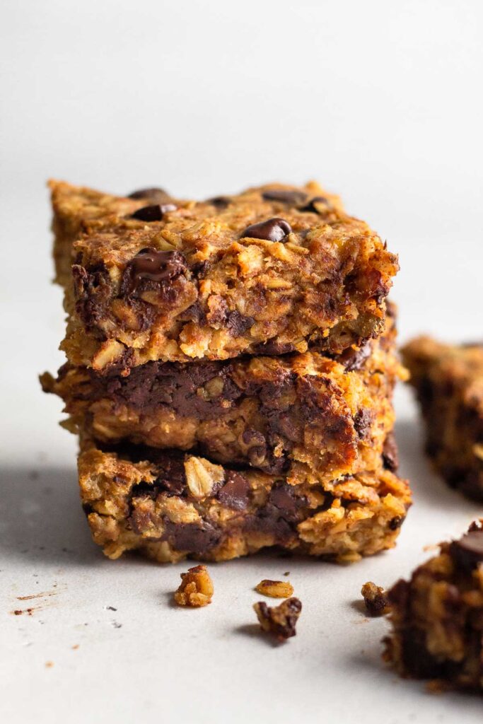 Three peanut butter oatmeal chocolate chip bars stacked on top of each other. Next to them are some crumbs and 2 more pieces off to the side.