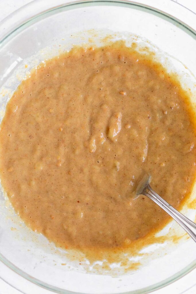 A mixing bowl with a mixture of mashed banana, peanut butter, and milk in it.