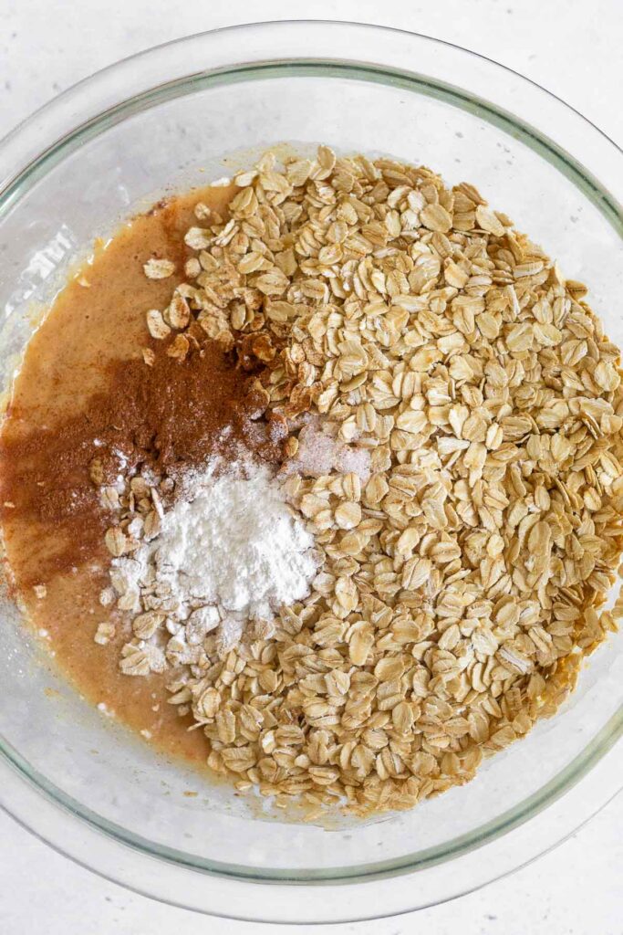 A mixing bowl with rolled oats, cinnamon, and baking powder on top of a wet batter before it is mixed.