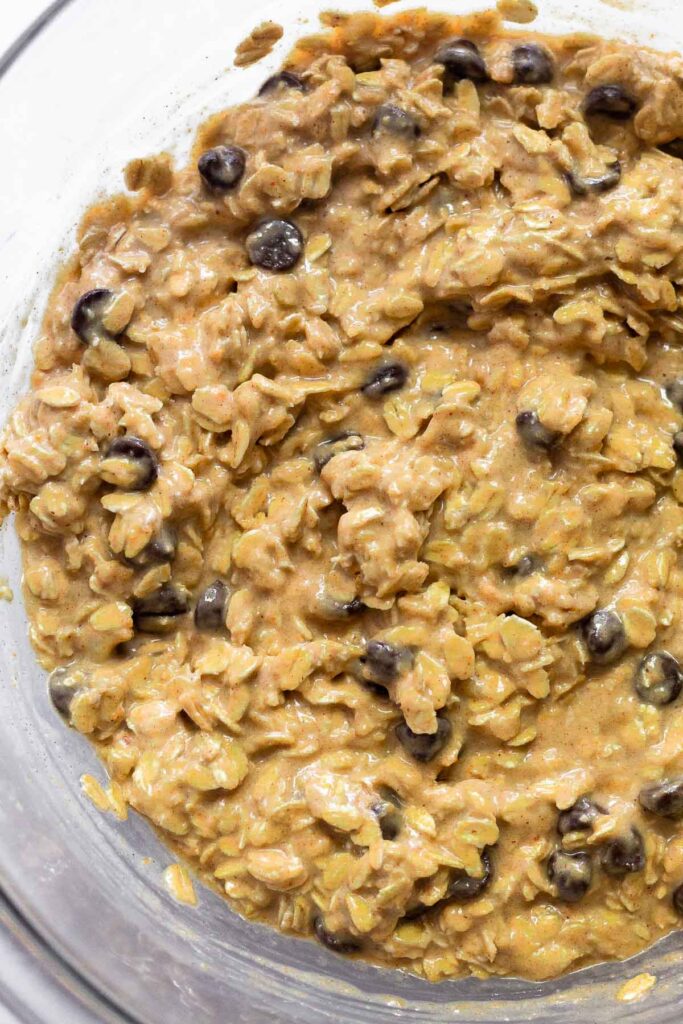 Close up of a mixing bowl filled with a batter of oats, chocolate chips, and mashed banana.