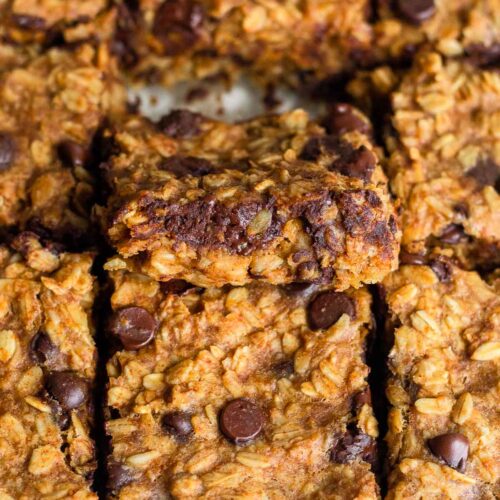A baking dish of oatmeal chocolate chip bars in it with the middle one slightly resting on the one in front of it so you can see the inside of it.