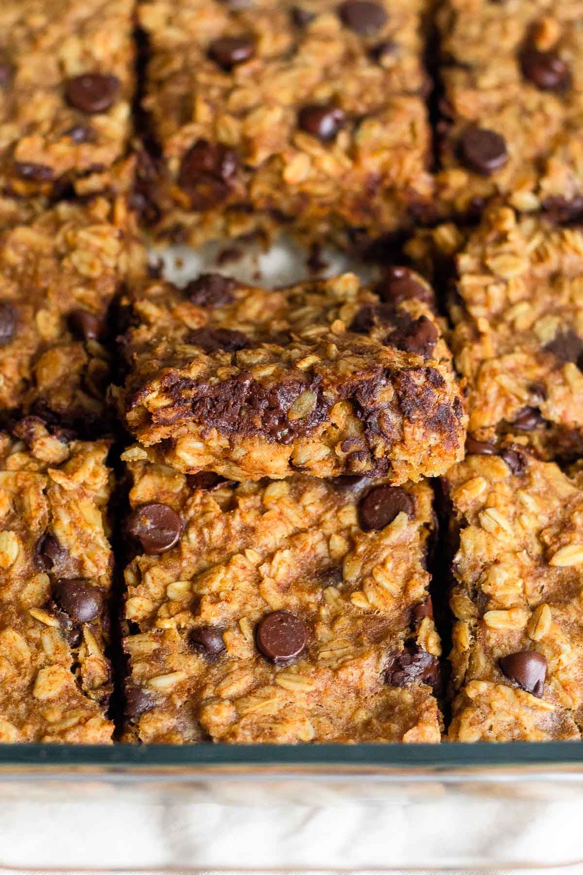 A baking dish of oatmeal chocolate chip bars in it with the middle one slightly resting on the one in front of it so you can see the inside of it.