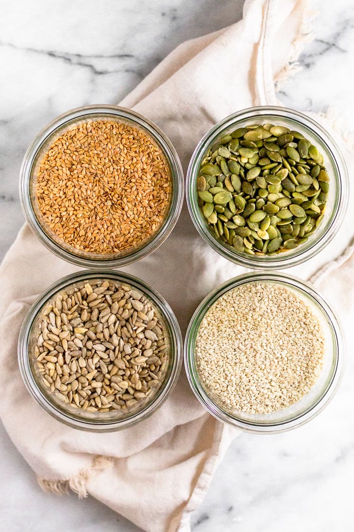 Four jars with different seeds in the (flax, pumpkin, sesame, and sunflower) for seed cycling to get your period back naturally.