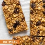 Overhead shot of oatmeal raisin bars lined up on parchment paper with one bar pulled slightly away from the other bars.