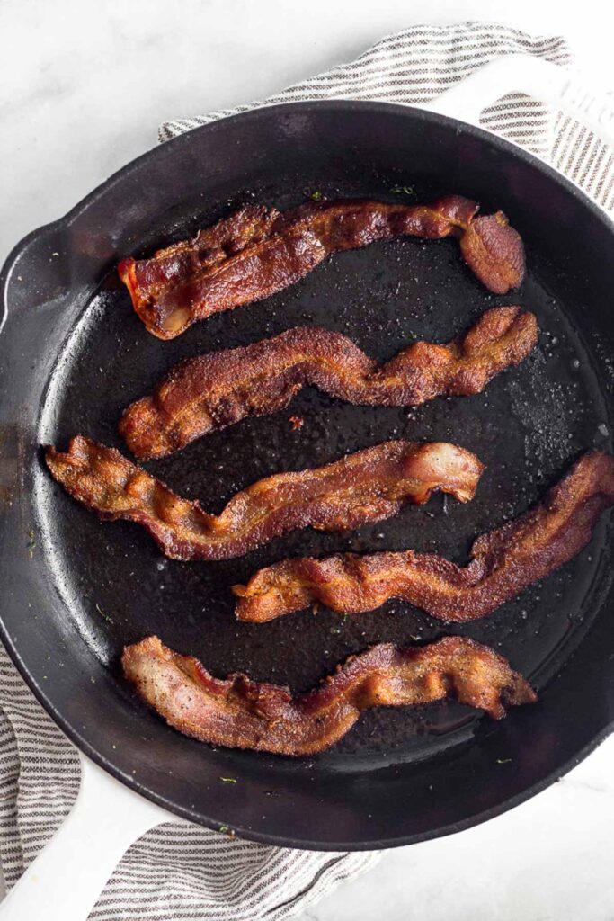 Cast iron skillet with 5 pieces of cooked bacon in it.