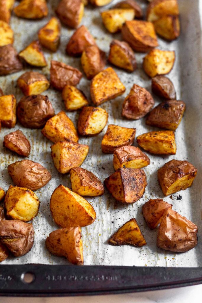 Baking sheet lined with parchment paper filled with chopped roasted red potatoes.