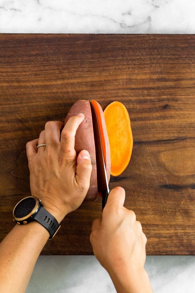 Overhead shot of someone cutting a sweet potato lengthwise.