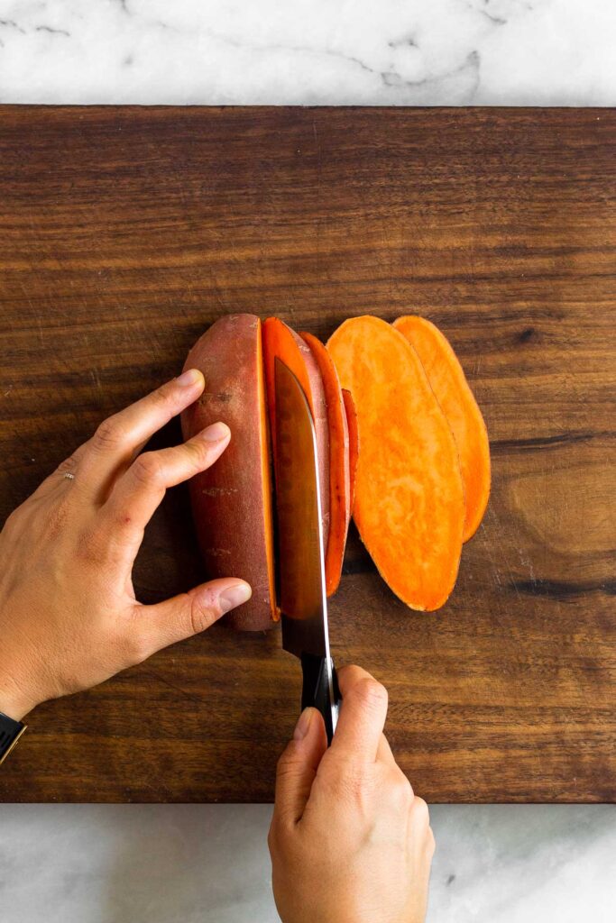 Overhead shot of someone cutting a sweet potato lengthwise into 1/2 inch pieces.