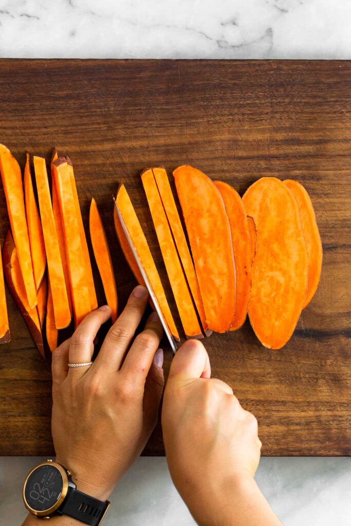 Overhead shot of someone cutting homemade sweet potato fries on a cutting board.