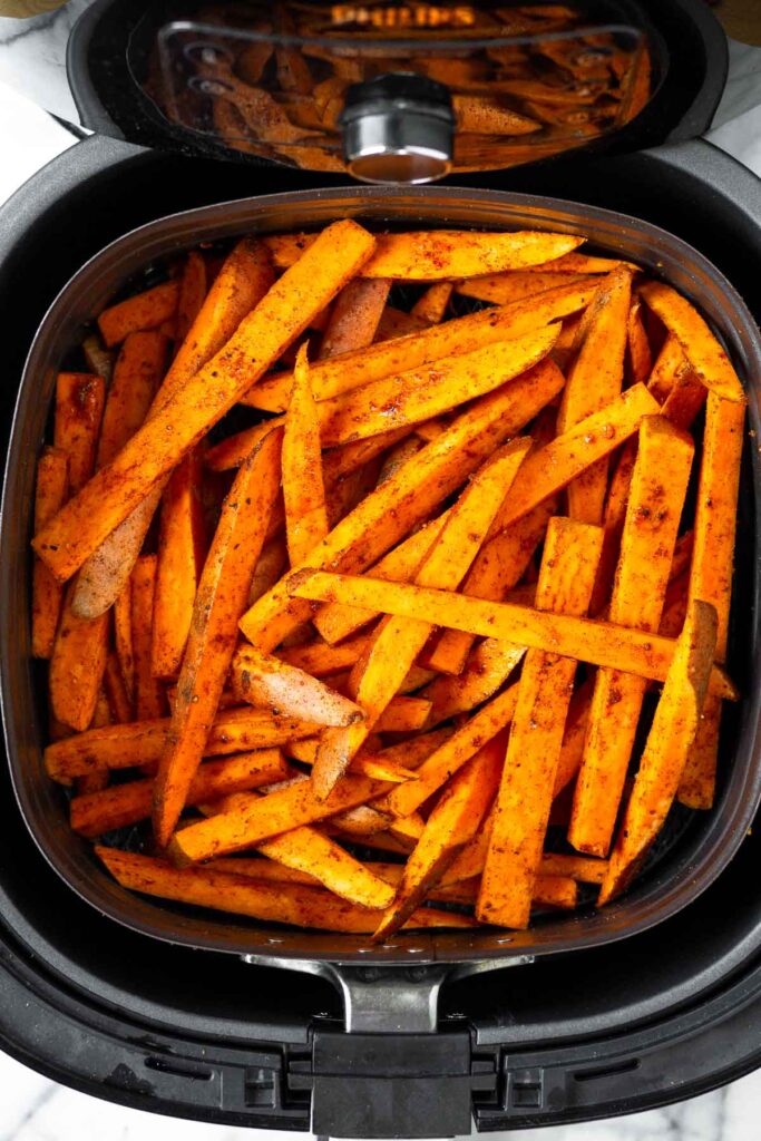 Raw sweet potato fries in an air fryer basket.