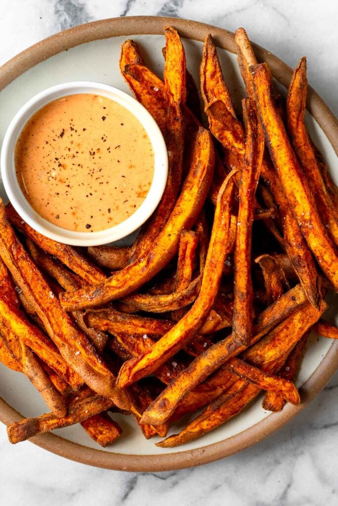 White plate filled with air fryer sweet potato fries with a small bowl of dipping sauce