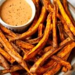 Air fryer sweet potato fries on a plate with a ramekin of dipping sauce.