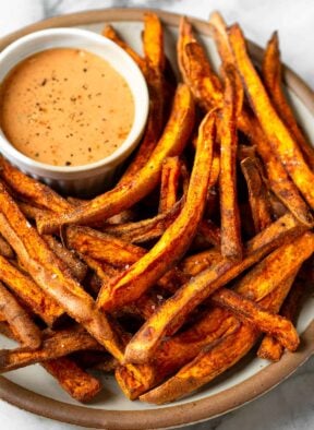 Air fryer sweet potato fries on a plate with a ramekin of dipping sauce.