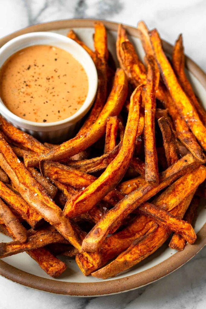 Air fryer sweet potato fries on a plate with a ramekin of dipping sauce.