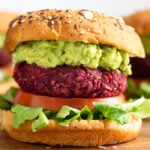 Close up of a beet burger on a bun with lettuce, tomato, and mashed avocado.