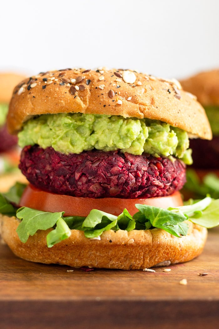 Close up of a beet burger on a bun with lettuce, tomato, and mashed avocado.