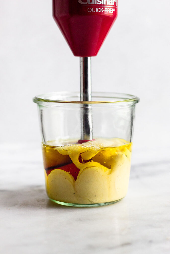 A large jar with an immersion blender in it making homemade mayonnaise.