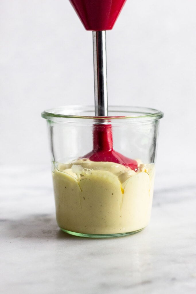 Homemade mayo in a large jar being made with an immersion blender.