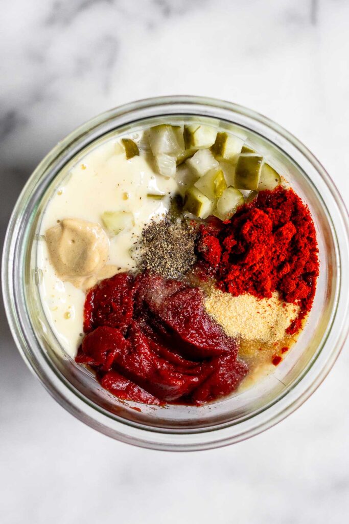 A jar with homemade mayo, tomato paste, mustard, chopped pickles, and spices before it is mixed.