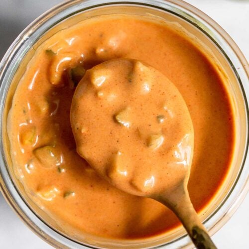 Burger sauce in a jar with a spoon overtop holding some. Off to the side is a bowl of diced pickles.