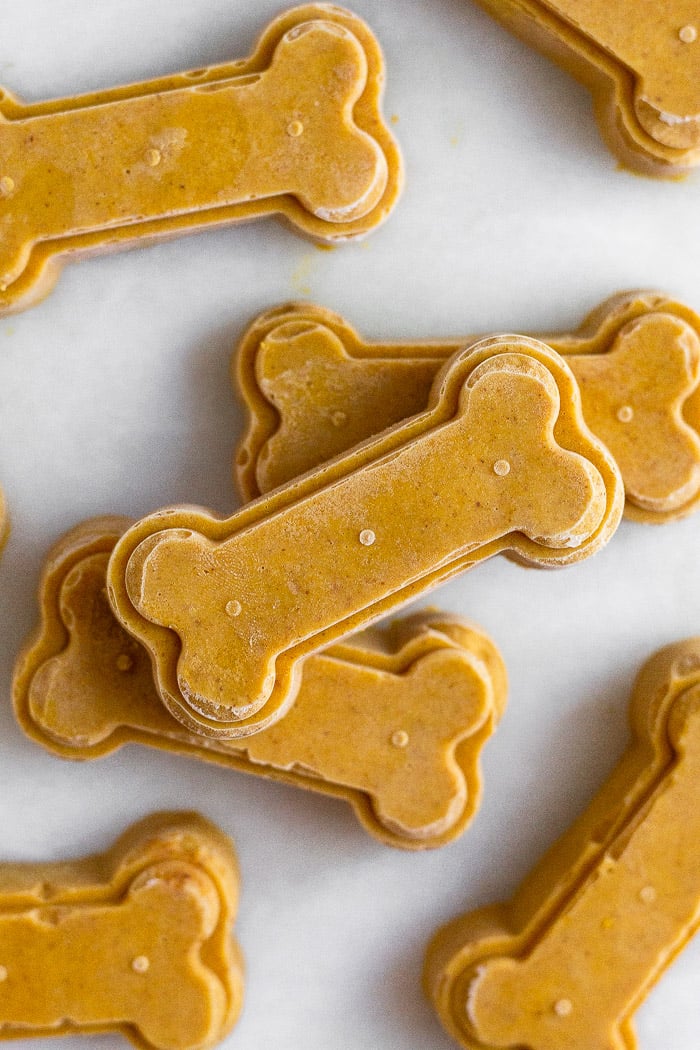 Frozen pumpkin peanut butter dog treats spread out on a white counter top with some stacked on top of each other.