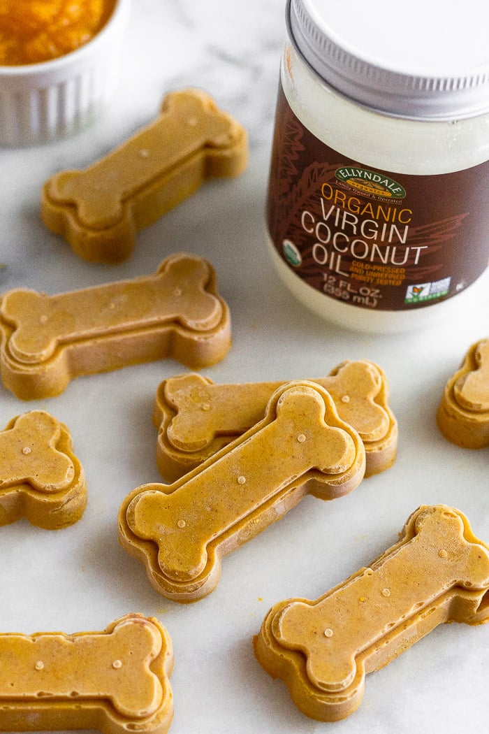 Homemade dog treats on a white counter with a jar of coconut oil and small dish of pumpkin behind them.