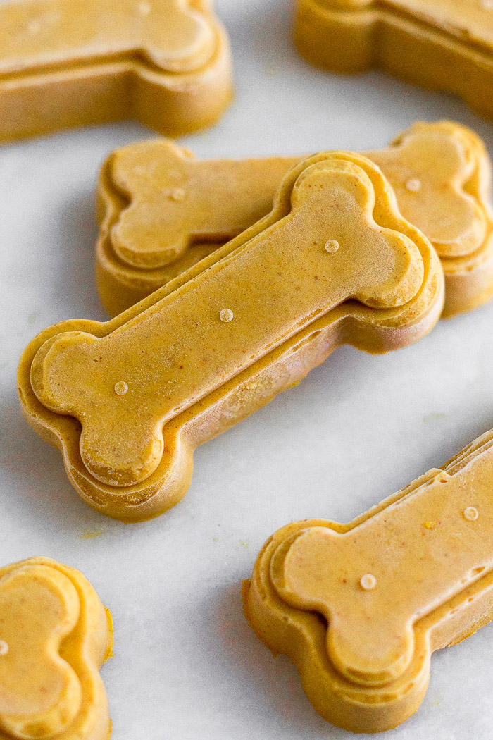 Healthy pumpkin peanut butter dog treats on a white counter with some stacked on top of each other.