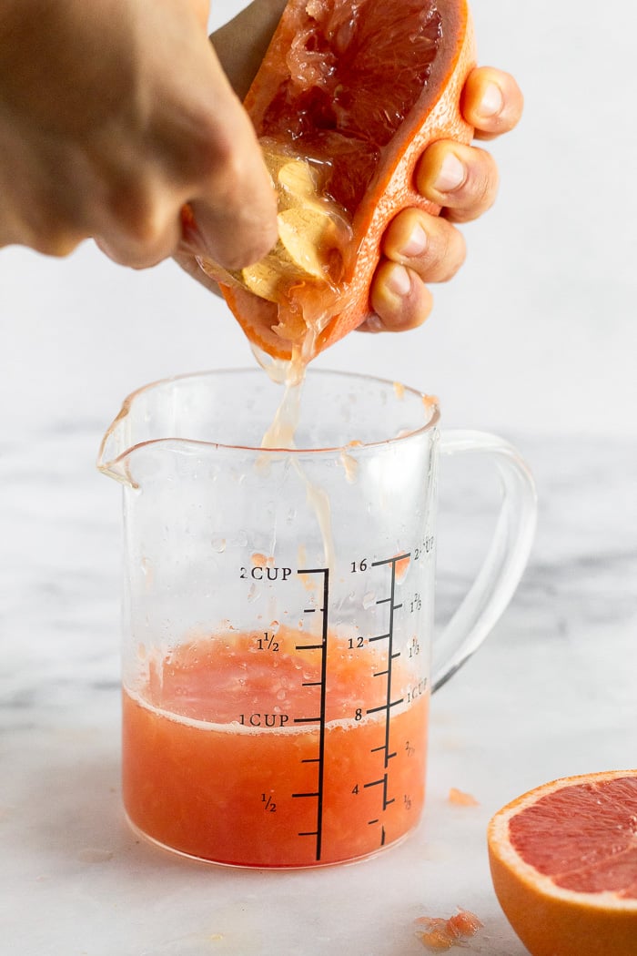 Measuring glass with someone squeezing grapefruit juice into it.