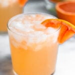 Close up of a grapefruit crush with a grapefruit wedge in it. Behind it is another one and half a grapefruit.