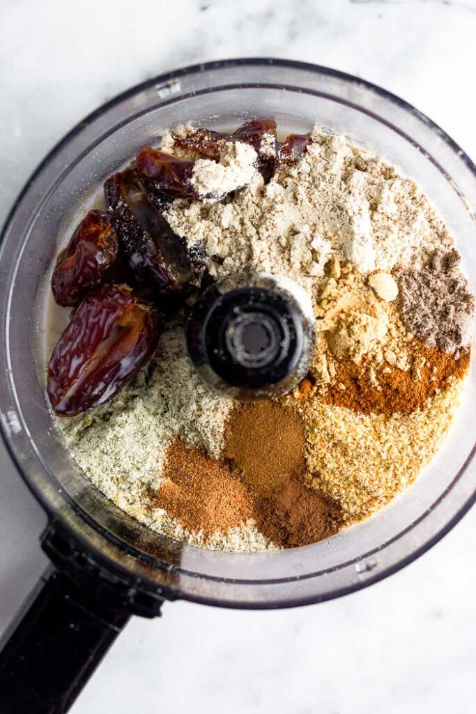 Overhead shot of a food processor filled with sound seeds, dates, protein powder, spices, and almond milk.
