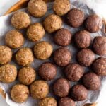 Seed cycling energy balls on a plate. On the side of it is two containers of seed cycling seeds.