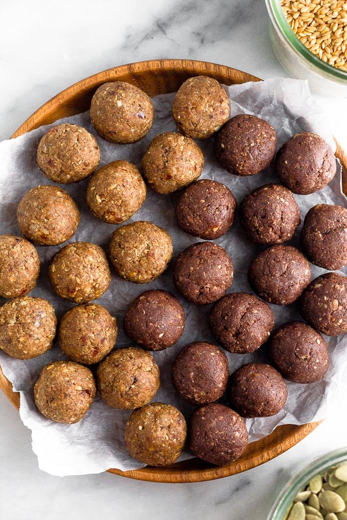 Seed cycling energy balls on a plate. On the side of it is two containers of seed cycling seeds.